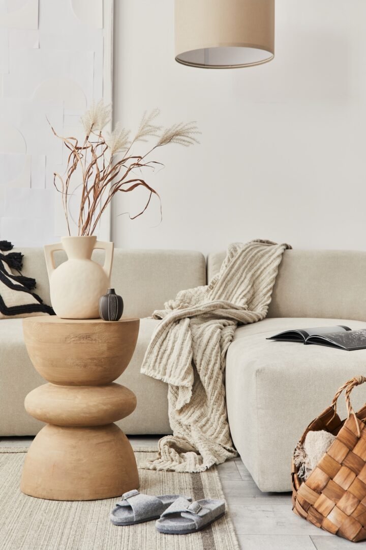 Stylish composition at fancy interior withwooden coffee table, dried flowers in vase, slippers, basket and book in modern home decor. Details. Template.